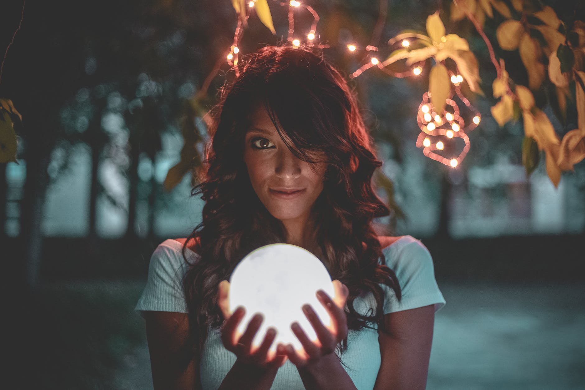 woman holding lighted glass ball under string lights